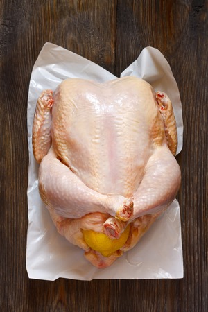Fresh raw whole chicken stuffed lemon for cooking on wooden board. Top view.の写真素材