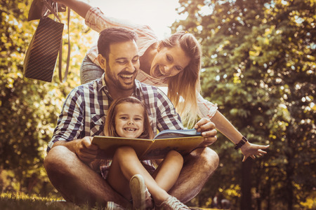 Happy family with one child in meadow reading book together.の写真素材