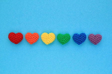 Crochet hearts rainbow colors on blue background. LGBT flag gay pride community, equal rights movement and gender equaluty concept. Valentine's Day idea for postcard, banner, poster, advertisingの写真素材