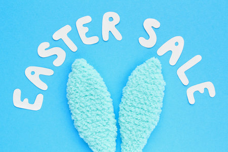 Colorful bunny ears and lettering Easter sale on blue background. Easter sale banner with easter decorated fur ears. Top view, flat lay creative concept for advertising, poster, magazine, web pageの写真素材