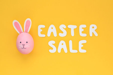 Colorful egg with funny bunny and lettering Easter sale on yellow background. Easter sale banner with easter decorated egg. Top view, flatlay creative concept for postcard, poster, magazine, webの写真素材