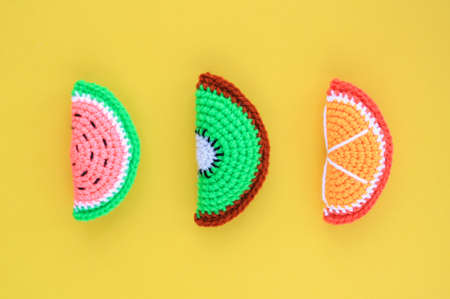 Colorful crochet handmade slices of watermelon, kiwi and orange on yellow background. Summer...
