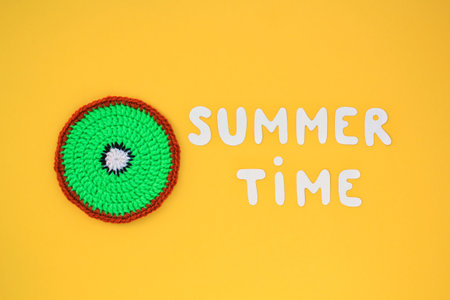 Colorful crochet handmade slice of kiwi and lettering Summertime on yellow background. Hello Summer vacation creative tropical bright minimal food concept. Flatlay, top view holiday compositionの写真素材