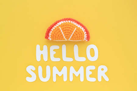 Colorful crochet handmade slice of orange and lettering Hello Summer on yellow background. Summertime vacation creative tropical bright minimal food concept. Flatlay, top view holiday compositionの写真素材