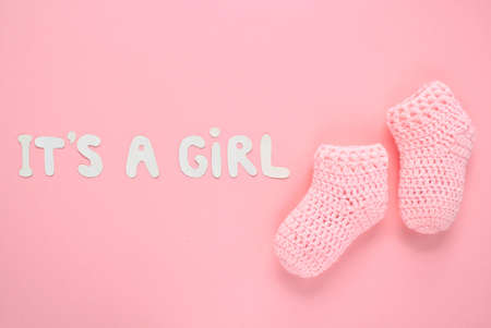 It's a girl lettering, crochet baby booties on pink background. Baby girl birth, new life, family concept. greeting card idea for newborn. Pregnancy announcement. Flat lay, top viewの写真素材