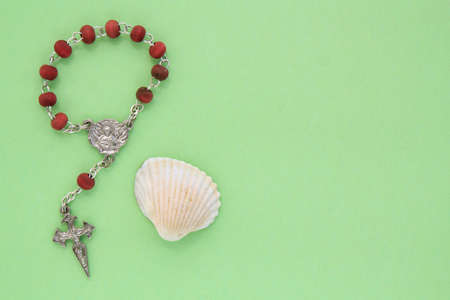 Pilgrim scallop shell and wooden rosary beads with crucifix cross with copy space on green...