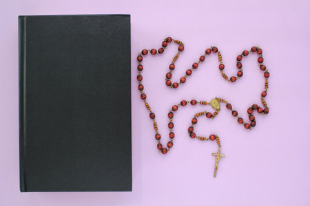 Rosary wooden beads and crucifix christian cross on holy bible book on violet background. catholic...