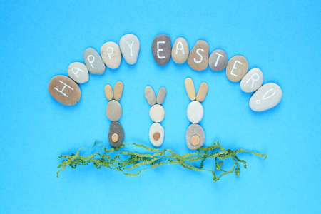Bunny and Happy Easter lettering on pebbles with green recycle paper on blue background. Ecological,...