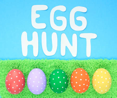 Egg hunt letters on blue background and coloured eggs with polka dot on green grass background. Easter greeting card, invitation, banner, poster sale. Flatlay, top view holiday conの写真素材
