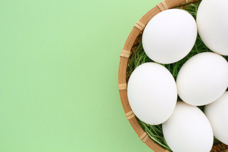 Fresh chicken eggs in wooden rattan wicker basket on green background. Natural healthy nutrition...