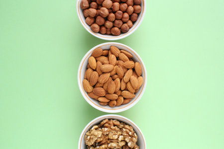 Assortment of nuts in ceramic bowls. Walnut, hazelnut, almond on green background. Organic raw food...