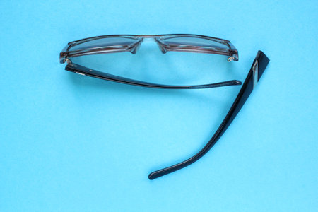 Old broken eyeglasses with damaged legs on blue background. Poor eyesight. Reuse and repair concept. idea of health. failure optic eyewear. Breakage of vision correction glasses. Cの写真素材