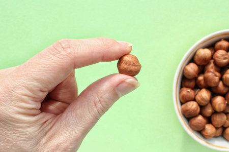 Woman holding organic hazelnut in her hand on green background. Nutrition healthy food choice...