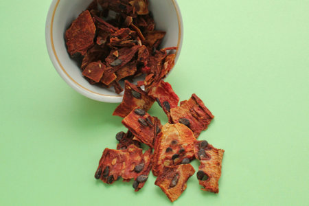 Slices of red dehydrated watermelon pulp pieces in white bowl on green background. Dried fruit chips. Organic natural healthy snack food. Homemade vegan diet. Home cooked superfoodの写真素材