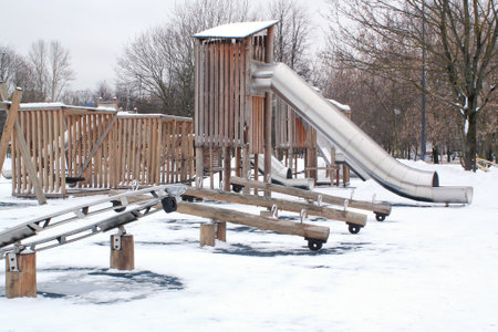 Wooden playground made of natural eco-friendly material in public city park with snow at winter time. Modern safety children outdoor equipment. Winter activities. Children rest andの写真素材