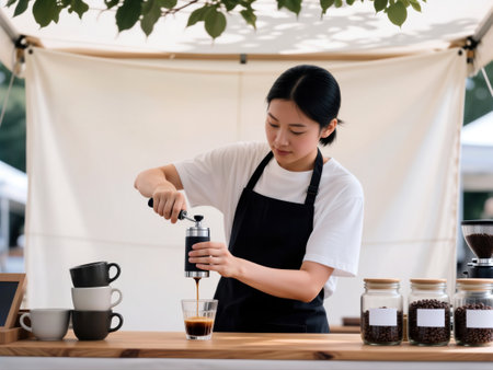 Young female barista uses manual portable coffee press at outdoor market stall.の素材