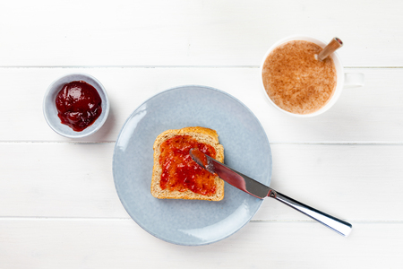 toast with strawberry jam on a blue plate and cup of cacao on a white wooden backgroundの写真素材
