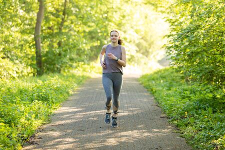 young woman running in a forest and makes fitness workoutの写真素材