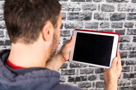 young man uses a tablet with stone wall