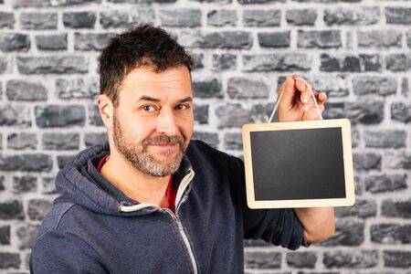 man holds blackboard in his hands in front of a stone wallの写真素材