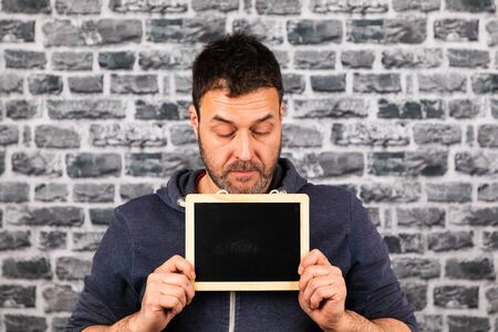 man holds blackboard in his hands in front of a stone wallの写真素材
