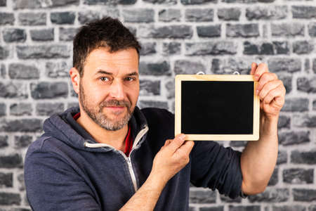 man holds blackboard in his hands in front of a stone wallの写真素材