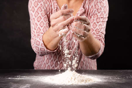 Female hands kneading dough with flour on dark background, closeupの写真素材