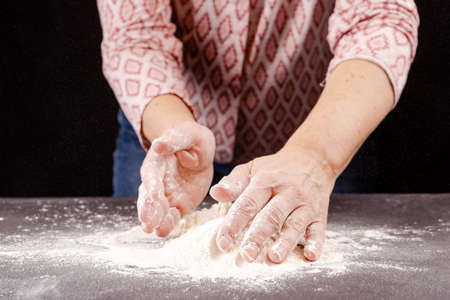 Woman's hands knead the dough on a black background. Close-up