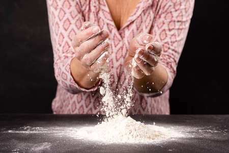 Female hands kneading dough with flour on black background, closeupの写真素材