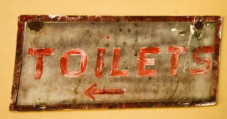 old rustic sign showing way to toilets on yellow wall with red letteringの写真素材