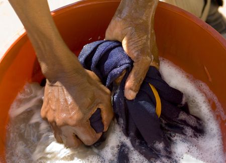 two african hands washing blue shirt in a red plastic tubの写真素材