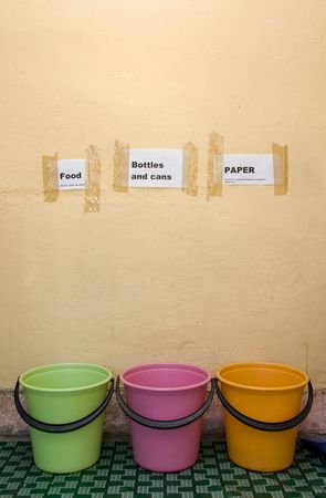 three colored plastic buckets in a farm kitchen with signs posted against the wall to recycle and separate food,bottles,cans and paperの写真素材