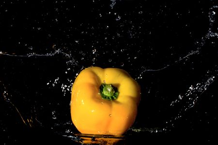 whole yellow pepper splashing in water with droplets flying around against black backgroundの写真素材