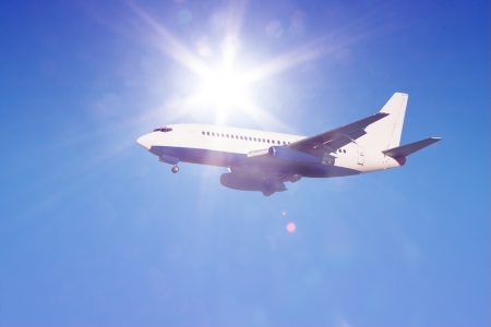passenger jet in flight against clear blue sky with sun rays and flares landing gear downの写真素材