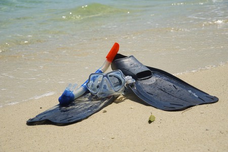 Snorkeling equipment (mask, snorkel and fins) on white sand beach with ocean on backgroundの写真素材