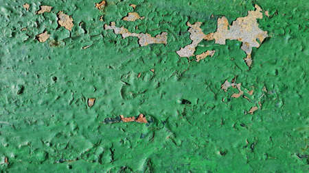Old green paint is cracked and falling off the metal sheet due to exposure to natureの写真素材