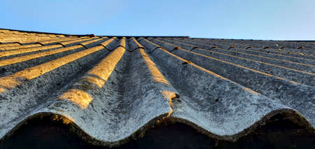 Old moss-covered and damaged roof shingles in several places. Roof shingles illuminated by the rays...