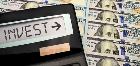 Invest in new projects with minimal risk. Calculator with the words "invest" on the screen against the background of a large number of bills of 100 us dollarsの写真素材
