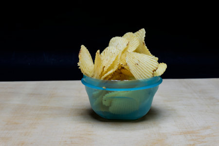 Salted Potato Wafers Chips in lite Cyan bowl on table, isolated in black background, Heap of Wafers Chipsの写真素材