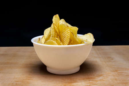 Salted Potato Chips in White bowl on table, isolated in black background, Heap of Chipsの写真素材
