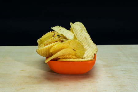 Salted Potato Wafers in Small Saffron Square Bowl On Wooden Table, Heap of Wafers, Copy Space, Heap of Chips, Side Viewの写真素材
