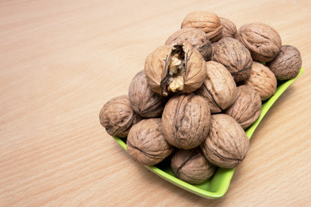 Fresh Walnuts in a Vibrant Green Bowl on a Wooden Surface, This image captures the rustic charm of...