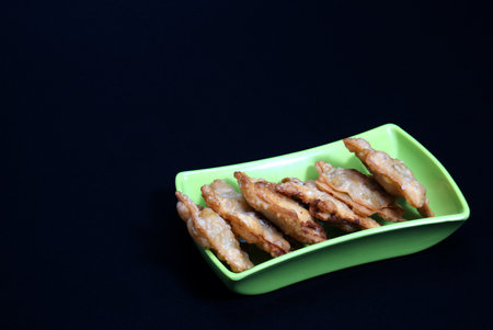 A green dish featuring fried chicken atop Aloo Puff Pastry, served with a side of tomato sauce.
