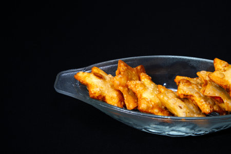 A glass bowl overflowing with golden, crispy samosas, featuring a crunchy exterior and rich,...