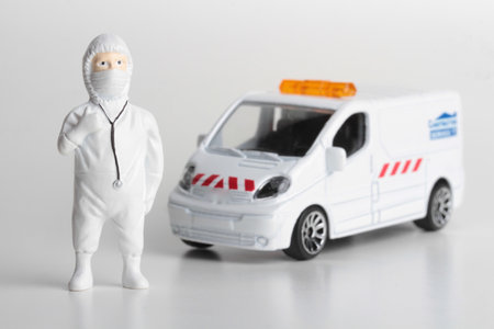 Miniature people wearing a hazmat suit and a medical mask standing near an ambulanceの写真素材
