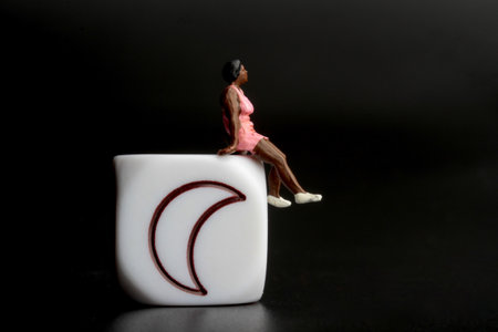 miniature woman sitting on a white block with the moon in the backgroundの写真素材