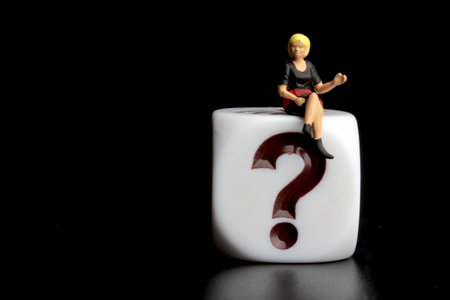 Miniature people sitting on a white cube with question mark on black backgroundの写真素材