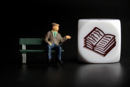 Miniature people: old man sitting on a bench with a book symbolの写真素材