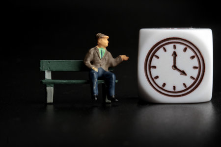 Miniature people: old man sitting on a bench and holding a clockの写真素材