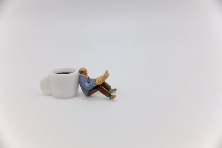 miniature people sitting on a cup of coffee on white background.の写真素材